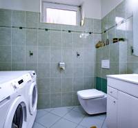 Koupelna v rodinném domě s pračkou, sušičkou, umyvadlem a toaletou, zelené obklady.