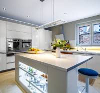 Kuchyně v rodinném domě s centrálním ostrůvkem, bílými skříňkami a spotřebiči.