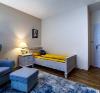 Pokoj rodinného domu s křeslem, postelí, nočním stolkem a podlahou s dřevěným dekorem.