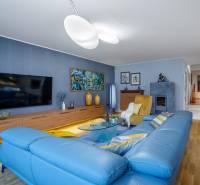 Obývací pokoj v rodinném domě s modrou sedačkou, podlahou s dřevěným dekorem a televizorem.