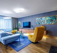 Obývací pokoj v rodinném domě s modrou sedačkou, žlutým křeslem a podlahou s dřevěným dekorem.