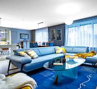 Obývací pokoj v rodinném domě s modrou sedačkou, skleněným stolkem a podlahou s dřevěným dekorem.