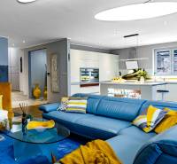 Obývací pokoj v rodinném domě s modrou sedačkou a kuchyní, podlaha s dřevěným dekorem.