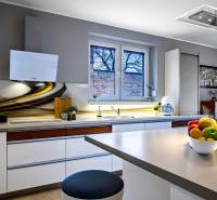 Kuchyně v rodinném domě se stylovou deskou, bílými skříňkami a dekoracemi na okně.