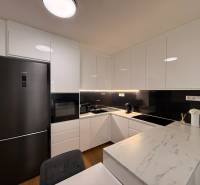 Kuchyně 2pokojového bytu s bílými skříňkami a podlahou s dřevěným dekorem.