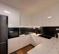 Kuchyně v 2-pokojovém bytě s lesklou bílou linkou a podlahou s dřevěným dekorem.