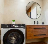Koupelna v 1-pokojovém bytě s pračkou, kulatým zrcadlem a skříňkou.