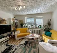 Obývací pokoj v 2pokojovém bytě s podlahou s dřevěným dekorem, žlutou sedačkou a dekoracemi.