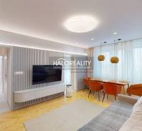 Obývací pokoj v 3-pokojovém bytě s TV na stěně, sedačkou a jídelním stolem.