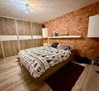 Ložnice v 2pokojovém bytě s postelí, úložným prostorem a podlahou s dřevěným dekorem.