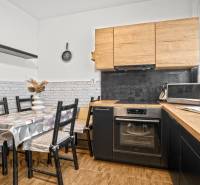 Kuchyně s dřevěným dekorem, jídelním stolem a spotřebiči ve 3pokojovém bytě.