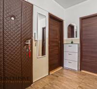 Předsíň s podlahou s dřevěným dekorem, šatníkovou skříní a zrcadlem v 3-pokojovém bytě.