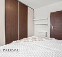 Ložnice v 3pokojovém bytě s postelí, vestavěnou skříní a minimalistickými policemi.