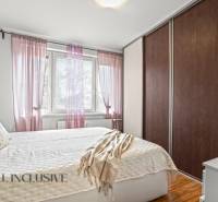 Ložnice v 3pokojovém bytě s postelí, skříní a dekorativními polštáři, podlaha s dřevěným dekorem.