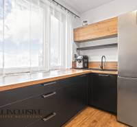 Kuchyně v 3-pokojovém bytě s velkým oknem, černými skříňkami a podlahou s dřevěným dekorem.