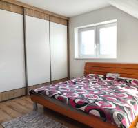 Ložnice v rodinném domě obsahuje postel, skříň a podlahu s dřevěným dekorem.