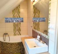 Koupelna v rodinném domě s vanou, umyvadlem, zrcadlem a mozaikovou výzdobou.