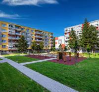 Dětské hřiště mezi bytovkami na Sládkovičově ulici ve Fiľakovu, obklopené zelení.