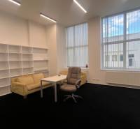 Kanceláře s černým kobercem, nábytkem, policovými systémy a velkými okny.