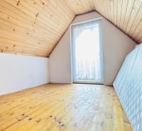 Podkrovní pokoj na chatě s podlahou s dřevěným dekorem a střešním oknem.