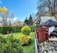 Zahrada u chaty v Partizánském s altánkem, upravenými keři a stromy.