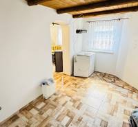 Interiér v chatě s podlahou s dřevěným dekorem, pračka, obloukový vstup do kuchyně.