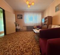 Obývací pokoj v rodinném domě s kobercovou podlahou, nábytkem a záclonami.