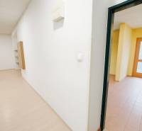 Bílá chodba v obchodních prostorách s podlahou s dřevěným dekorem a místnost s dlažbou.