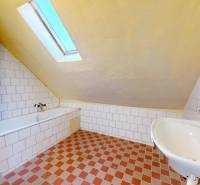 Koupelna v rodinném domě s vanou, umyvadlem a šikmým stropem.