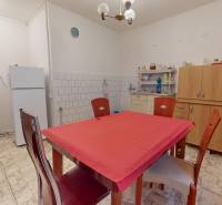 Kuchyně v rodinném domě s bílou lednicí, mikrovlnkou a jídelním stolem.