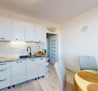 Kuchyně v 3-pokojovém bytě s podlahou s dřevěným dekorem, jídelním stolem a bílými skříňkami.