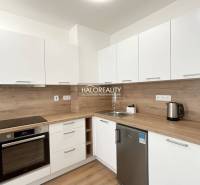 Kuchyně v 1-pokojovém bytě s podlahou s dřevěným dekorem a bílými skříňkami.