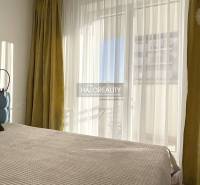 Světlá ložnice v jednopokojovém bytě s velkým oknem a závěsy.