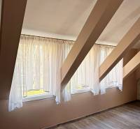 Interiér podkroví s okny a podlahou s dřevěným dekorem.