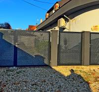 Kovová brána u budovy v Komárně na štěrkovém pozemku u domu.