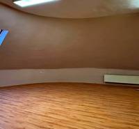 Podkrovní pokoj s oknem, radiátorem a podlahou s dřevěným dekorem.