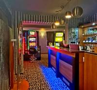 Interiér budovy s hracími automaty, pultem a nápoji na policích.