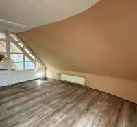 Interiér budovy s podlahou s dřevěným dekorem a šikmou světle hnědou stěnou.