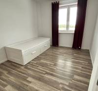 Pokoj s postelí, podlahou s dřevěným dekorem a velkým oknem ve 3pokojovém bytě.