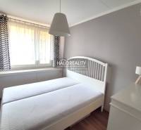 Ložnice v dvoupokojovém bytě s bílým nábytkem a jemnými závěsy.