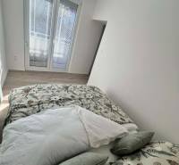 Světlá ložnice v 2-pokojovém bytě s dekorativními polštáři a podlahou s dřevěným dekorem.