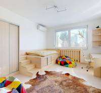 Pokoj v 5 a více pokojovém bytě s postelí, barevnými polštáři a pracovním stolem.