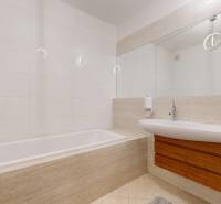 Koupelna v 5 a více pokojovém bytě s vanou a umyvadlem, obklady a velké zrcadlo.