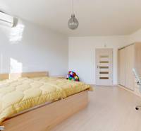 Světlá ložnice v bytě s 5 a více pokoji s postelí, psacím stolem a skříní.