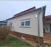 Rodinný dům v Hurbanově se světlou fasádou a červenou střechou, obklopený keři.