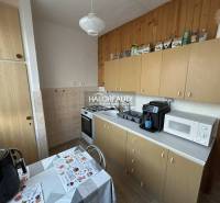 Kuchyně v 2-pokojovém bytě s dřevěným dekorem, včetně spotřebičů a jídelního stolu.