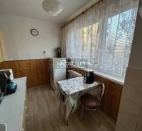 Kuchyně s dřevěným dekorem v 2pokojovém bytě. Jemné záclony, jídelní stůl, kávovar.