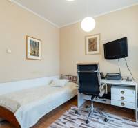 Pokoj ve 4pokojovém bytě s postelí, pracovním stolem a televizí na zdi.