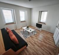 Obývací pokoj v rodinném domě s pohovkou, televizí a podlahou s dřevěným dekorem.