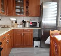 Kuchyně s dřevěným dekorem, sporákem, lednicí a jídelním stolem ve 3-pokojovém bytě.